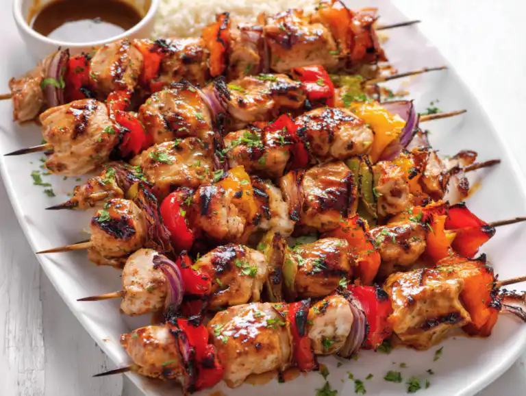 A top-down view of a platter with perfectly grilled chicken kabobs, red and yellow bell peppers, zucchini, and red onions.